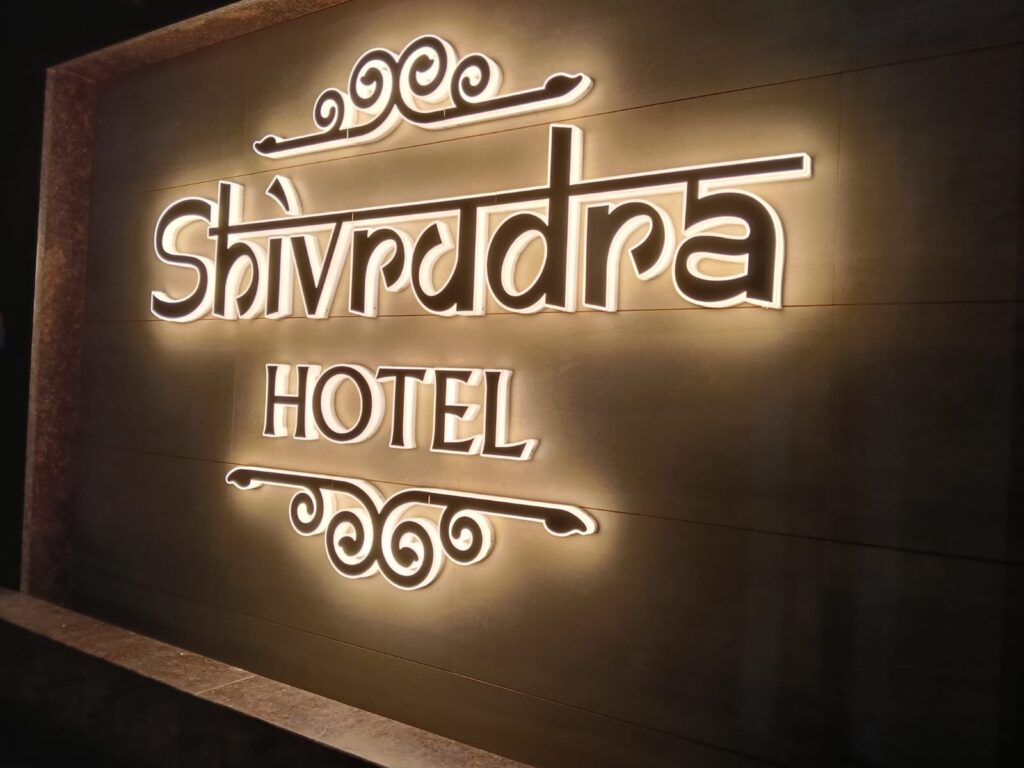 3D LED Board: Elegant 3D LED illuminated acrylic sign board displaying शिवेंद्र होटेल Shivendra Hotel with decorative flourishes on wooden textured background